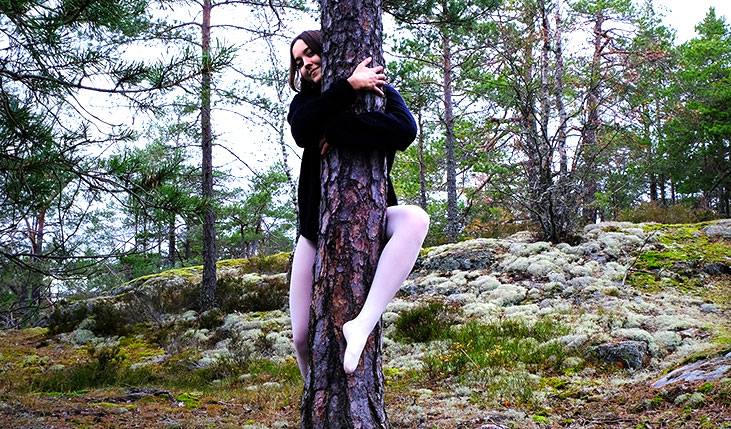 Ein Frau in weißer Strumpfhose umklammert einen Baum