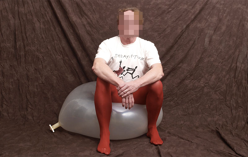 Ein Mann in einer roten Strumpfhosde sitzt auf einem Luftballon